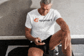 a man wearing an appmart t-shirt sits on the floor looking at his phone