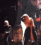 a woman is dancing on stage with a man playing a guitar in the background