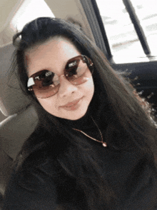 a woman wearing sunglasses and a black turtleneck is sitting in a car