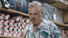 a man in a hawaiian shirt is standing in front of a shelf full of bags