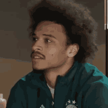 a man with an afro and a mustache is wearing a green jacket that says bayern