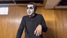 a man with white paint on his face is standing in front of a wood wall