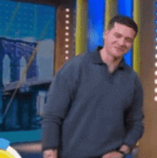 a man in a blue sweater is standing in front of a bridge on a television screen .