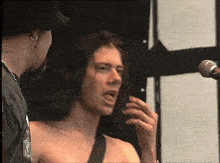 a shirtless man singing into a microphone with the letter k on his chest