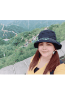 a woman wearing a black hat with the letter c on it stands in front of a mountain