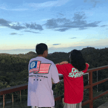 a man and a woman are standing on a balcony looking out over a body of water