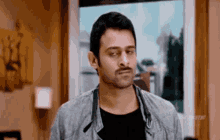a man with a mustache is standing in a room in front of a window .
