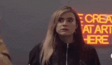 a woman in a black jacket is standing in front of a neon sign that says `` ne crea rea he '' .