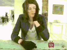 a woman wearing black gloves is sitting at a table with a tv on it