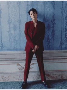 a man in a red suit and black shoes stands in front of a blue wall
