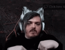 a man wearing headphones and fox ears is sitting in a chair and making a funny face .