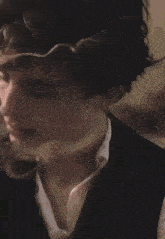 a close up of a person 's face with a white shirt and a black vest .