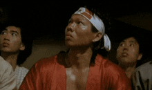 a man wearing a headband and a red robe is sitting in a room with other men .
