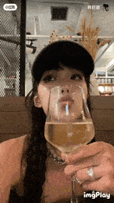 a woman wearing a hat and a ring is drinking from a glass of wine