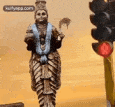 a statue of a deity is standing next to a red traffic light .