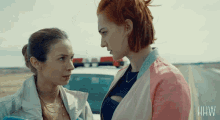 two women looking at each other in front of a police car that says hw