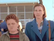 a woman in a blue coat stands next to a boy in a striped shirt