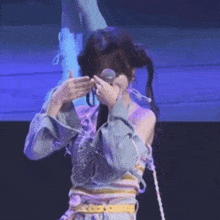 a girl is covering her face with her hands while holding a microphone .