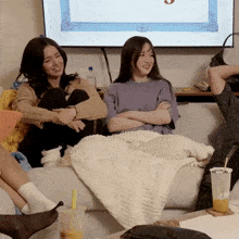 two women sit on a couch with their arms crossed in front of a flat screen tv