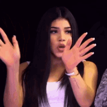a woman with long black hair is making a funny face with her hands up .