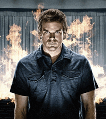 a man in a blue shirt stands in front of a burning curtain