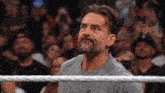 a man with a beard is standing in a wrestling ring with a crowd behind him .