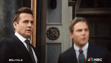 two men in suits are standing next to each other with the nbc logo in the background