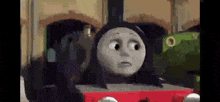 thomas the tank engine is making a sad face while standing next to another train .