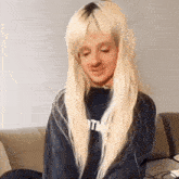 a woman with long blonde hair is sitting on a couch wearing a blue sweatshirt .