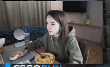 a woman is sitting at a desk with a bowl of food and a computer mouse