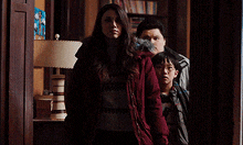 a woman in a red coat is standing next to two children in a dark room