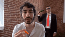a man with a beard is holding a carrot while another man in a suit holds a cucumber