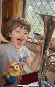 a young boy wearing a minion shirt holds a tuba