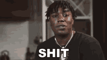 a man wearing a necklace and a black shirt is making a funny face and saying `` shit '' .