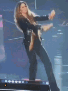 a woman in a black jacket is dancing on a stage with the letter l next to her