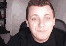 a man in a black shirt is sitting in a chair and smiling at the camera .