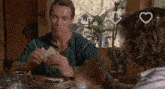 a man is eating a piece of bread while sitting at a table with another man .