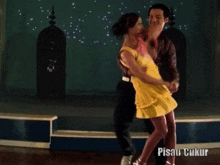 a woman in a yellow dress is dancing with a man in a brown shirt in a pisau ukur video