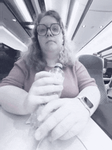 a woman sitting on a train holding a clear bottle that says rhine