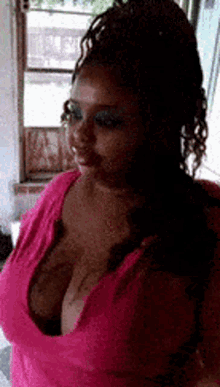 a woman in a pink tank top with a plunging neckline is standing next to a window .
