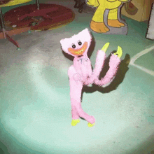 a pink stuffed animal with yellow feet is standing on a table