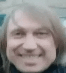 a close up of a man 's face with long hair smiling and making a funny face .