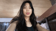 a woman with long black hair and a black tank top looks at the camera