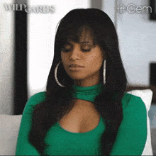 a woman in a green top and hoop earrings is sitting on a couch .