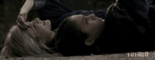 two women are laying next to each other on the ground and one of them is touching the other 's forehead .
