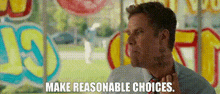 a man in a suit and tie is standing in front of a window with a sign that says make reasonable choices .
