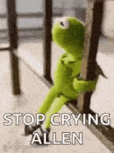 kermit the frog is sitting on a railing holding onto a pole .