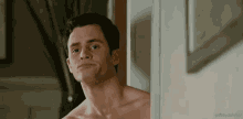 a shirtless man is leaning against a wall and looking at the camera .
