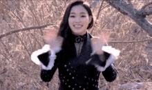 a woman wearing a black jacket and white gloves is standing in the woods .