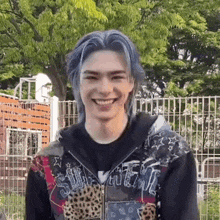 a young man with blue hair is smiling while wearing a leopard print jacket .